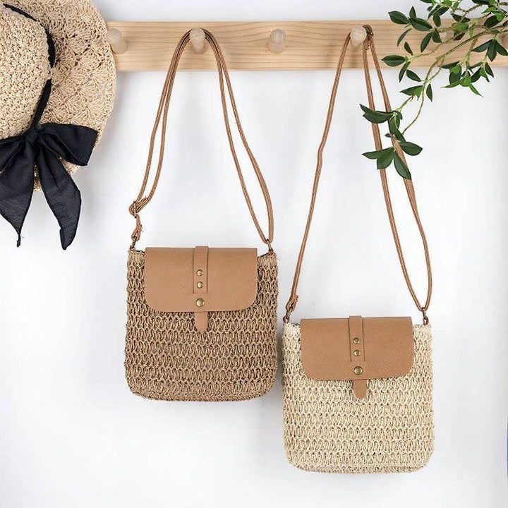 A Styled Collective patchwork straw crossbody bags with tan faux leather flaps hanging on a wooden wall hook.