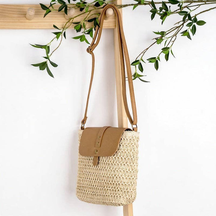 A Styled Collective patchwork straw crossbody bag with a tan faux leather flap and adjustable shoulder strap.