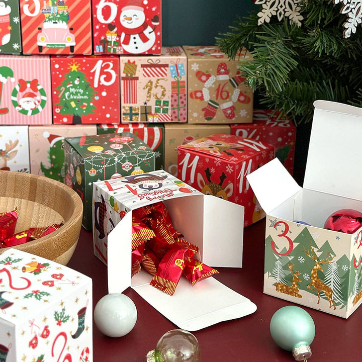 A collection of colorful Christmas advent boxes with various festive designs, including reindeer, Christmas trees, Santa Claus, and numbered doors, displayed on a dark red surface with a wooden bowl of wrapped gifts and a decorated Christmas tree in the background.